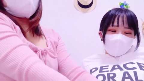 Media: Video of an Asian woman with a pink cardigan, mask, and straight hair, embracing a white-faced mannequin wearing a white shirt with \"PEACE FOR ALL\" in black letters.