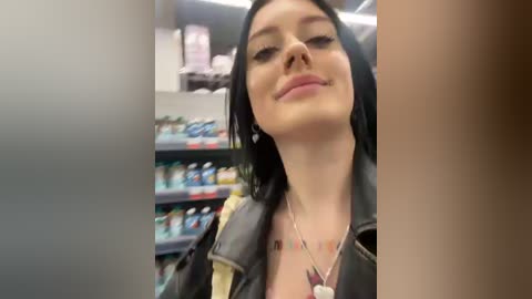 Media: A video of a woman with fair skin, black hair, and a confident expression, wearing a black leather jacket, standing in a grocery store aisle filled with colorful products.