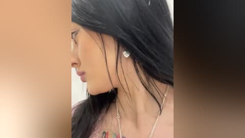 Media: A video of a young woman with long, straight black hair, wearing a silver necklace with a diamond pendant, and a light pink top, against a soft, gradient background.