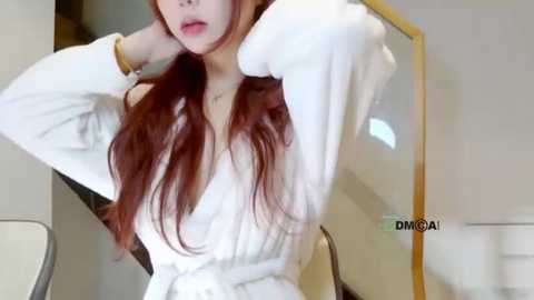 Media: A video of a young Asian woman with long, straight red hair, wearing a white off-shoulder dress, posing indoors with her hands behind her head.