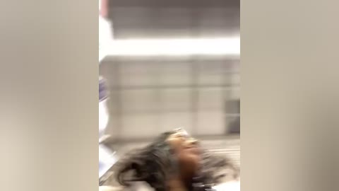 Media: A blurred video of a person with long, curly hair, lying on the ground in a dimly lit room with a large, bright window in the background.