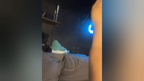 Media: A blurry video showing a dimly lit bedroom with a bed, a green pillow, a wooden shelf, and a blue moon-shaped nightlight on the wall.