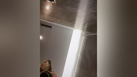 Media: Video of a modern, minimalist bathroom featuring a tall, narrow window with a sheer curtain, soft lighting, and a sleek, metallic ceiling.