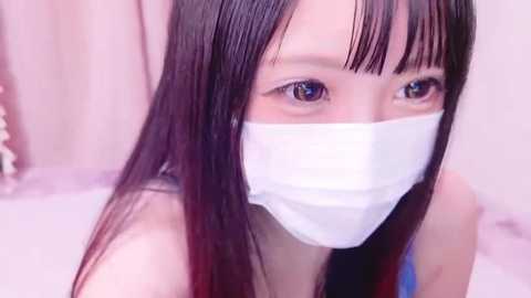 Media: A close-up video of an Asian woman with long, straight black hair, wearing a white surgical mask and a black top, looking directly at the camera with large, expressive eyes.