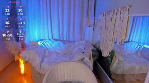 Media: A video of a dimly lit bedroom with a white canopy bed draped in soft, cream-colored blankets. A macrame wall hanging with tassels is mounted on the right wall, and blue LED lights create a soft, ambient glow.