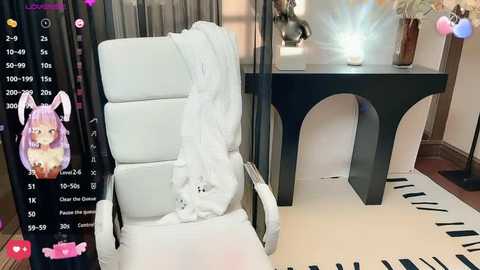 Media: A video of a white leather chair with a white blanket draped over it, next to a black, minimalist side table with a lit lamp, set in a cozy room with soft lighting.