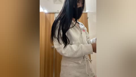 Media: Video of a woman in a white karate gi, with long black hair, partially covering her face, standing in a wooden-paneled changing room.