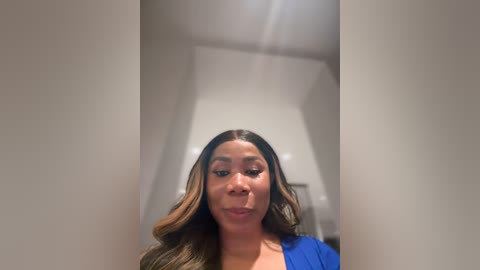 Media: A video of a Black woman with medium brown skin and long, wavy hair. She is indoors, wearing a blue top, with a blurry background.