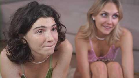 Media: Video of two women: one with curly black hair, wearing a green top, and the other with blonde hair, wearing a pink lace bralette, both smiling.