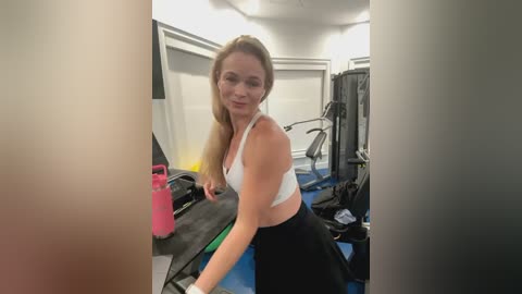 Media: Video of a fit, blonde Caucasian woman with fair skin and medium build, wearing a white sports bra and black skirt, working out in a gym.