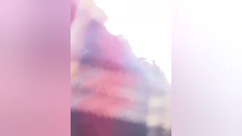 Media: Blurry video of a person with light skin, possibly male, wearing a dark shirt, partially visible in a soft, pastel-colored background with a hint of pink and purple tones.