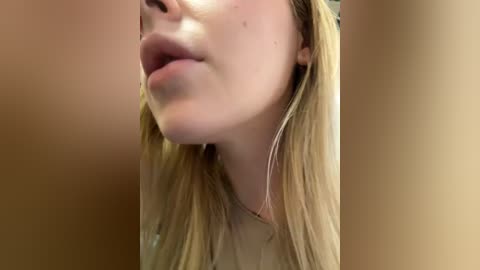 Media: Video of a close-up of a Caucasian woman with light skin and blonde hair, wearing a beige top, leaning in to kiss someone.