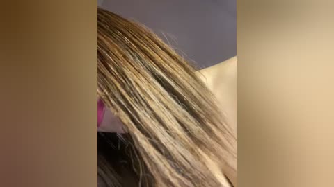 Media: Video of a person with long, straight, blonde hair partially covering their face, set against a blurred, beige and light blue background.