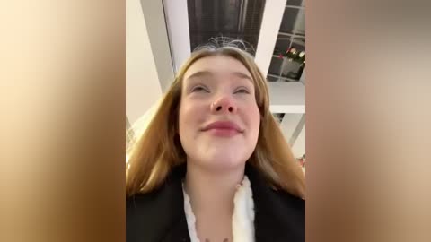 Media: A video of a smiling, fair-skinned woman with long, light brown hair, wearing a black blazer over a white blouse, taken from a low angle, with blurred faces in the foreground.