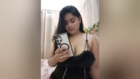 Media: Video of a young East Asian woman with long black hair, wearing a black lace bra, taking a mirror selfie indoors.