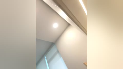 Media: Video of a modern, minimalist interior featuring a ceiling with a white recessed light and a beige wall. The image captures the clean, contemporary aesthetic with a focus on simplicity and functionality.