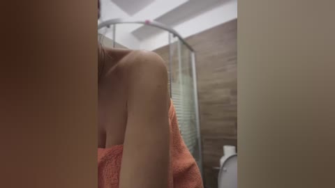 Media: Video of a nude woman with light skin, holding an orange towel in a modern bathroom with wooden walls and a glass shower.