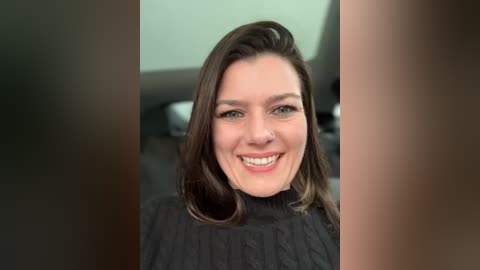 Media: A video of a smiling woman with shoulder-length dark brown hair, wearing a black turtleneck sweater, in a car interior with blurred background.