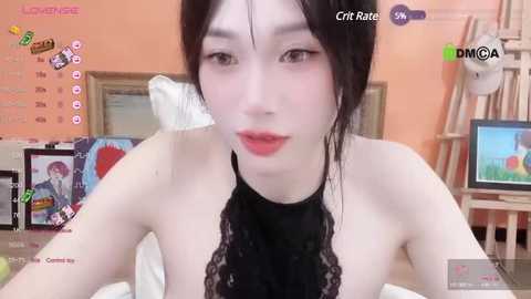 Media: Video of a young, slender, pale-skinned woman with black hair and pink lipstick, wearing a black lace top, in a cozy bedroom with a bed, paintings, and a TV.