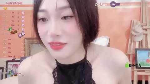 Media: A close-up video of an Asian woman with fair skin and dark hair, wearing a black lace top, sitting in a pink room with a calendar and computer.