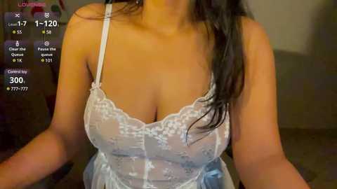 Media: Video of a woman with light brown skin, wearing a white lace bra, long dark hair, and a light blue dress, indoors, with a video call screen overlay.