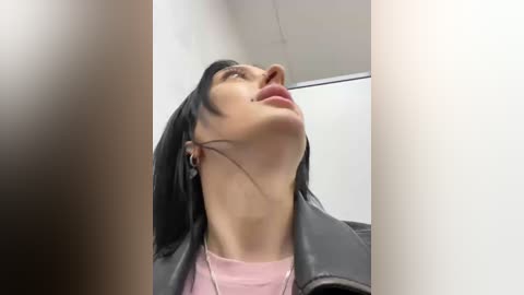 Media: A video of a woman with straight black hair, fair skin, and a light pink top, wearing a black leather jacket. She is looking upward, her head tilted back.