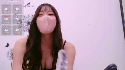 Media: A video of an East Asian woman with long black hair, wearing a black bra, blowing a large pink bubble gum bubble, set against a white wall with a gray chart and black butterfly artwork.