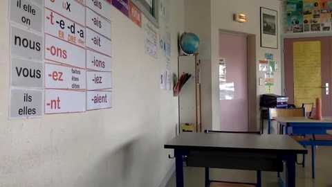 Media: Video of a classroom with a beige wall, black desk, blue chairs, French language posters, a globe, and a pink door.