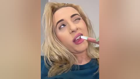 Media: Video of a blonde woman with fair skin, wearing blue lipstick, winking while brushing her teeth.