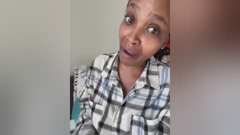 Media: A video of a young Black woman with a medium complexion and braided hair, wearing a plaid shirt. She has a neutral expression and is partially blurred.