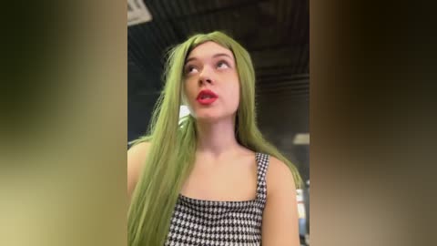 Media: Video of a young woman with long, neon green hair, wearing a black and white houndstooth dress, standing indoors with a ceiling fan visible in the background.