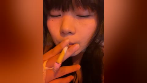 Media: A close-up video of an Asian woman with long, dark hair, eyes closed, smoking a cigarette, set against a blurred, warm-toned background.