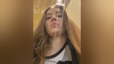 Media: A video of a young woman with long, light brown hair, wearing a black and white striped shirt, taken from a low angle, showing her slightly tilted head and upper body.