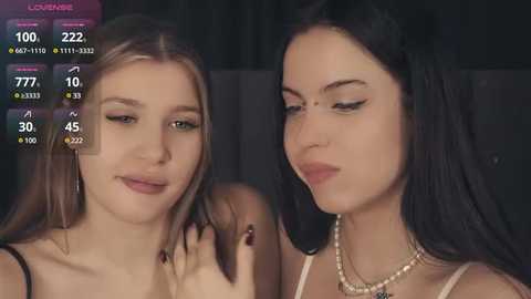 Media: Video of two young women, one with long blonde hair and the other with long black hair, wearing minimal makeup, against a dark background, with a \"LIVE\" watermark.