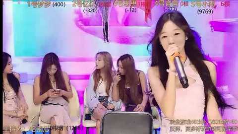 Media: Video of four young Asian women in colorful summer dresses, sitting on white chairs, in front of a stage with a vibrant, abstract background. One woman holds a microphone.