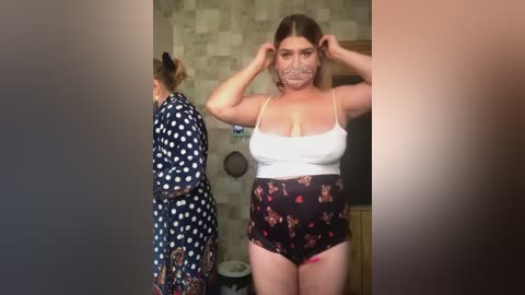 Media: A video shows two women in a bathroom; one in a polka-dot robe, the other in a floral top and shorts, both adjusting their masks.