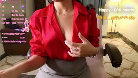 Media: Video of a woman in a red blouse, revealing cleavage, sitting in an office chair. Background includes a desk, flowers, and text overlay saying \"Happy 10k views.\