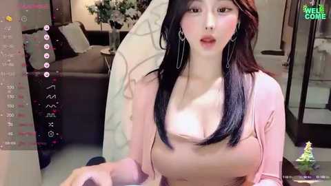 Media: Video of an East Asian woman with long black hair, wearing a low-cut pink top, and sitting in a modern living room with a gray couch, potted plants, and a Christmas tree.