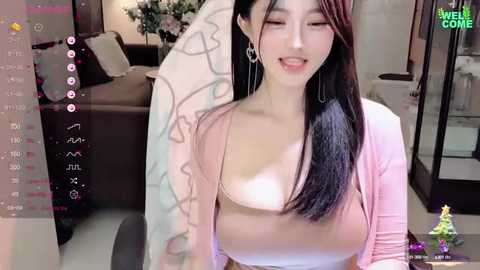 Media: A video of an Asian woman with long black hair, wearing a pink cardigan and white top, sitting in a modern living room with a brown couch.