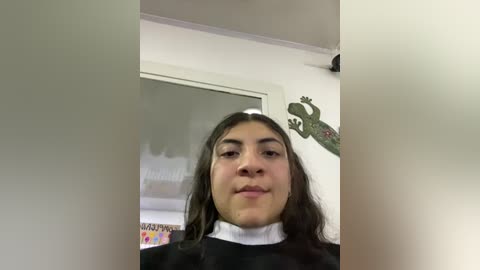 Media: A video of a Latina girl with long dark hair, wearing a black robe over a white turtleneck, standing in a brightly lit room with dinosaur wall art and colorful posters.