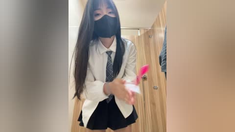 Media: Video of an Asian woman with long, straight black hair, wearing a white lab coat, black tie, black skirt, and black mask, holding a pink toy, in a wooden-walled hallway.