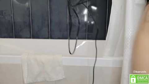 Media: Video of a white bathtub with black-tiled walls, a white towel draped over the faucet, and a black electrical cord hanging loosely.