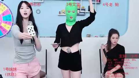 Media: Video of three young women, one wearing a green mask, in a colorful, modern room. One holds a dice, another a microphone, and a third smiles.