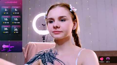 Media: Video of a fair-skinned young woman with brown hair in pigtails, wearing a white lace top, standing in a studio with a glowing ring light.