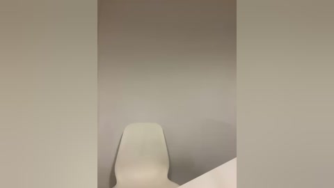 Media: A minimalist video of an empty, beige-walled room with a sleek, white, modern chair in the foreground, emphasizing clean lines and simplicity.