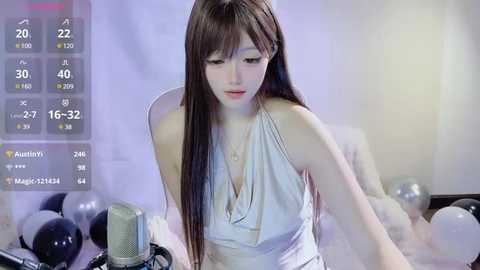 Media: A video of a young Asian woman with long brown hair, wearing a sleeveless white dress, singing into a microphone, surrounded by silver balloons, with a digital thermometer overlay displaying her temperature and stats.