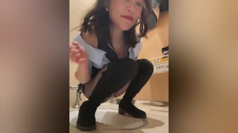 Media: A video of an Asian woman squatting in a bathroom, wearing a blue shirt, black skirt, and black thigh-high socks, with a white toilet behind her.