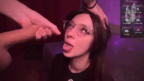 Media: Video of a woman with long black hair and glasses being touched by a hand on her head, wearing a black shirt, in a dimly lit room with purple lighting.