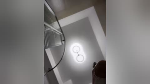 Media: Video of a modern interior, showing a spiral staircase with a white railing, a glowing circular light fixture, and a brown chair in the foreground.