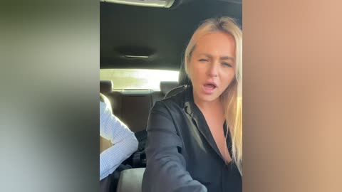 Media: Video of a blonde woman with long hair, wearing a black leather jacket, leaning out of a car window, mouth open in apparent surprise or shock.